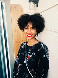 African-American woman with thick, curly, black, short hair, red lipstick and a black shirt with a floral print.