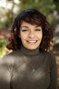 Young Latina female with medium length brown hair wearing a turtle neck and smiling.